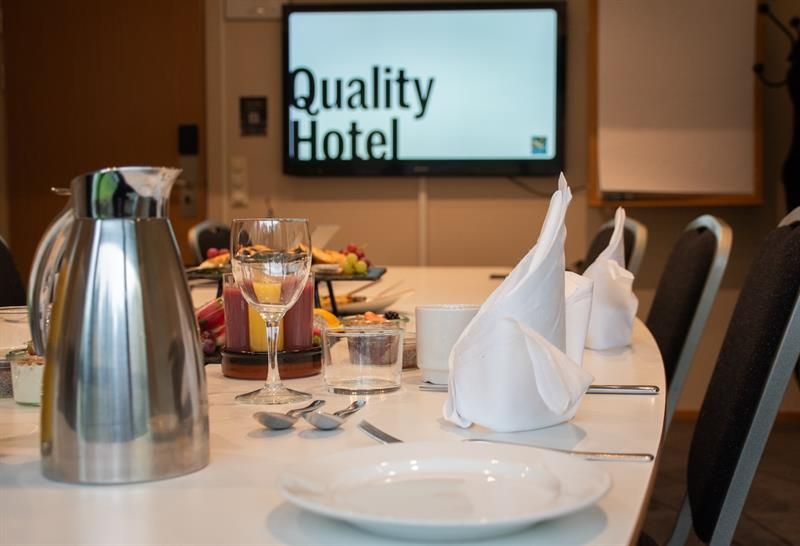 Pent dekket møtebord med tallerkener, servietter og servering, med skjerm i bakgrunnen.