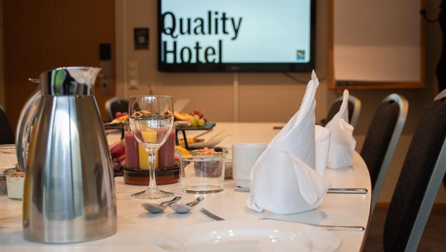 Pent dekket møtebord med tallerkener, servietter og servering, med skjerm i bakgrunnen.