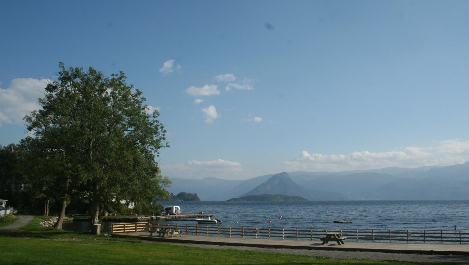 Utsikt frå Hardanger Feriesenter mot fjorden med benkar, brygge og fjell i bakgrunnen.