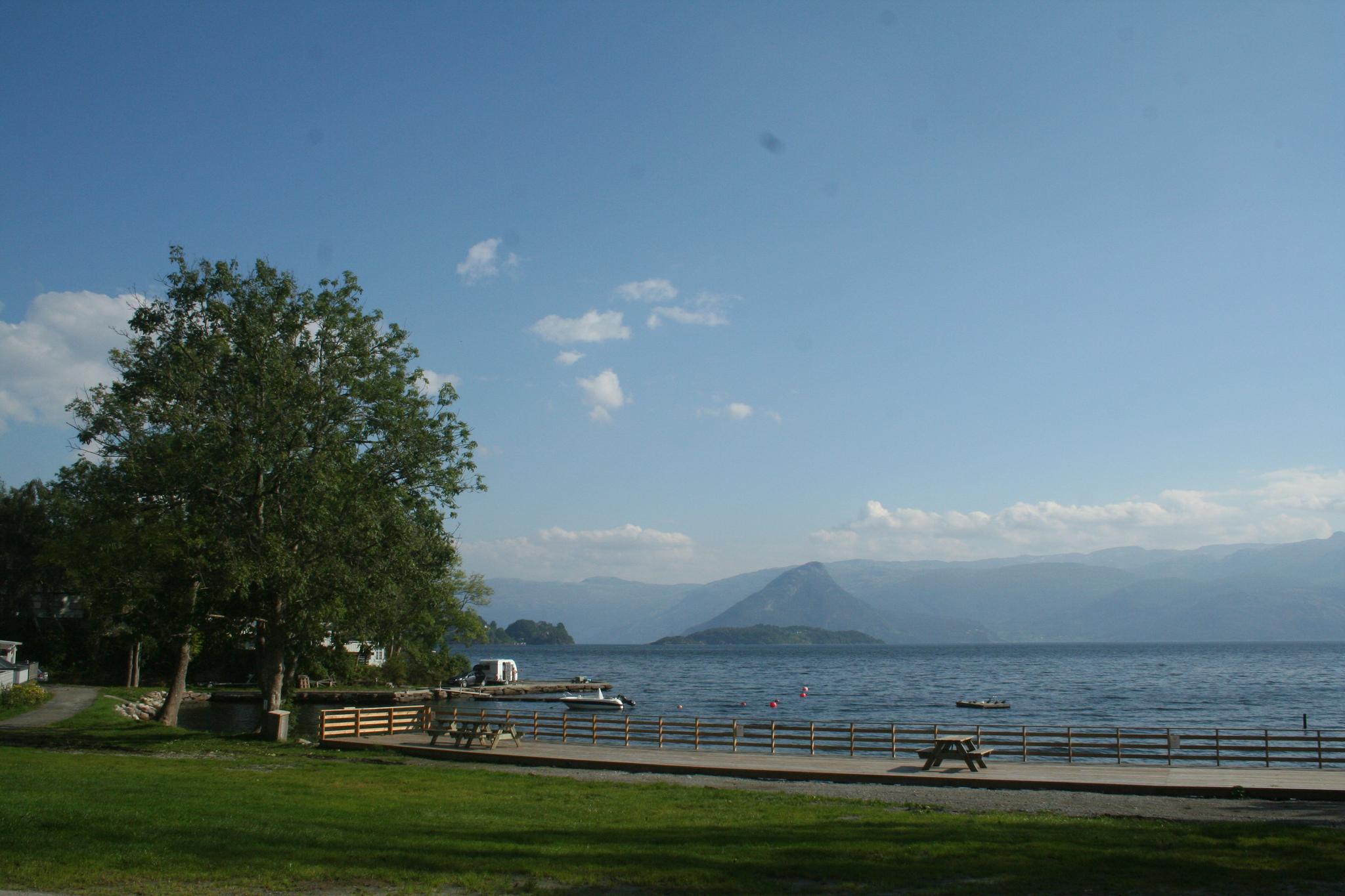 View from Hardanger Feriesenter towards the fjord with picnic benches, pier and surrounding mountains.