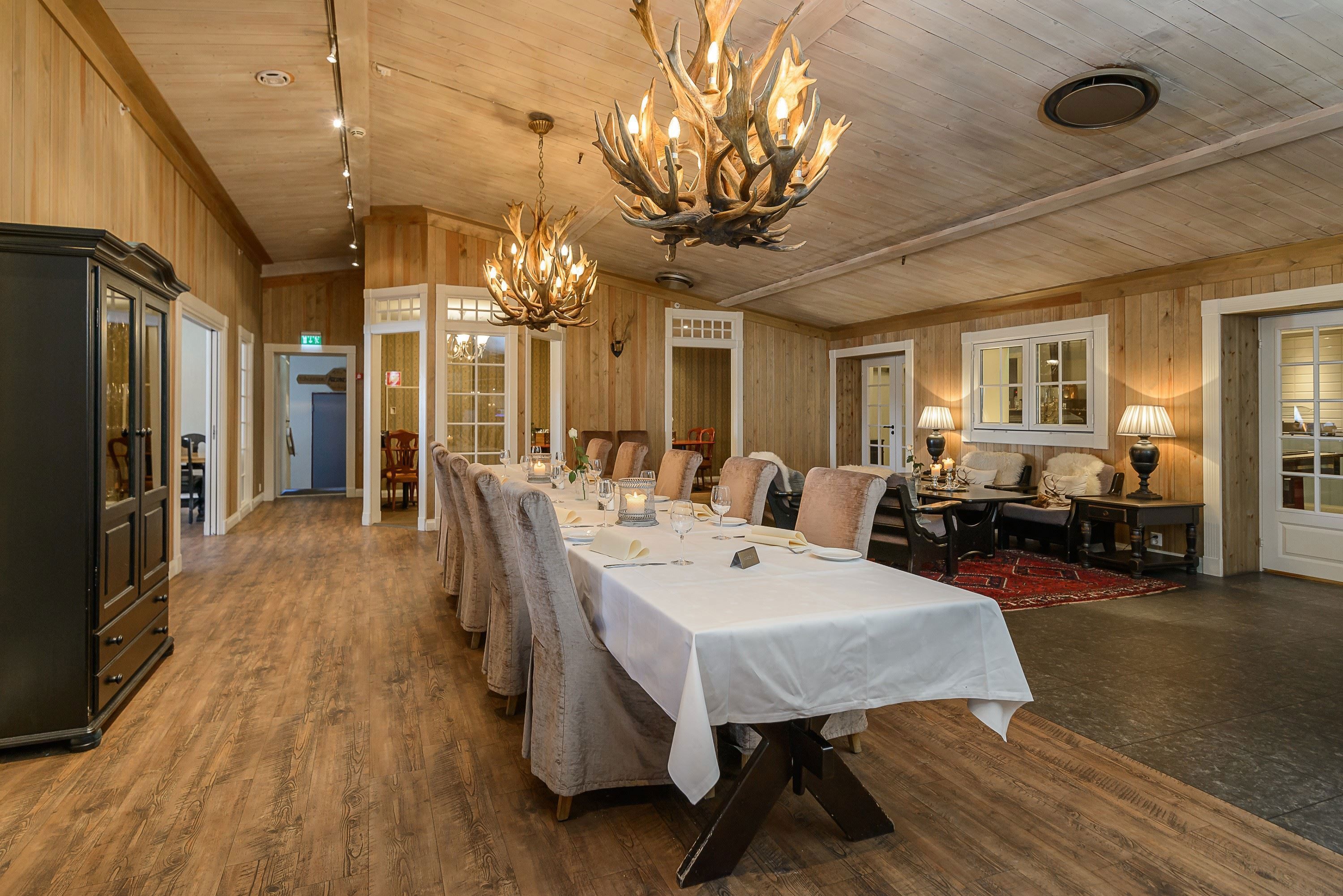 A long table with white tablecloths and chairs in a room with chandeliers.