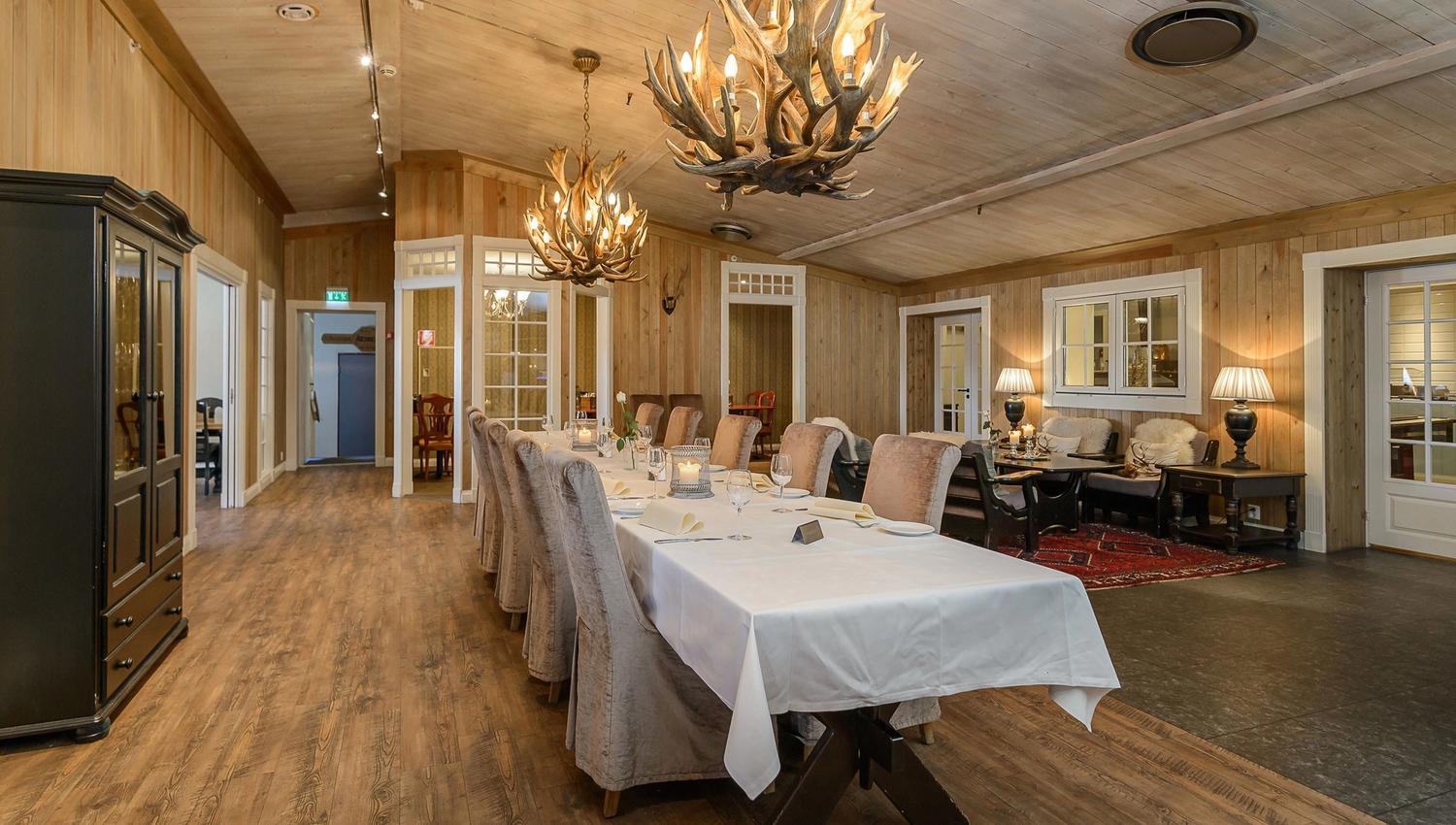 A long table with white tablecloths and chairs in a room with chandeliers.