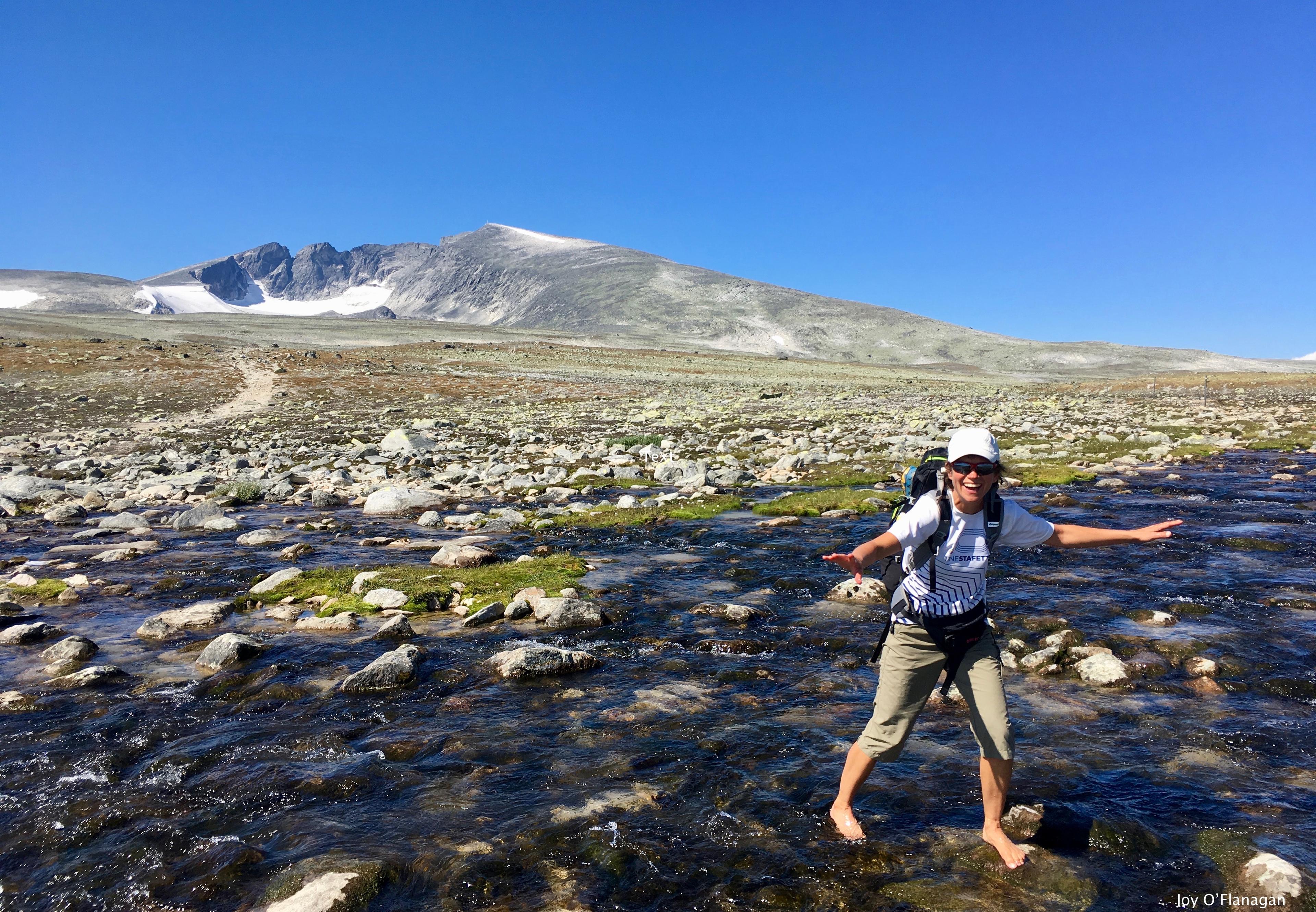 Female hiker crosses a river with Snøhetta in the background | Venabu Fjellhotell