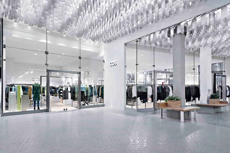 Hvitt butikkinteriør med høyt tak, søyler og benker.