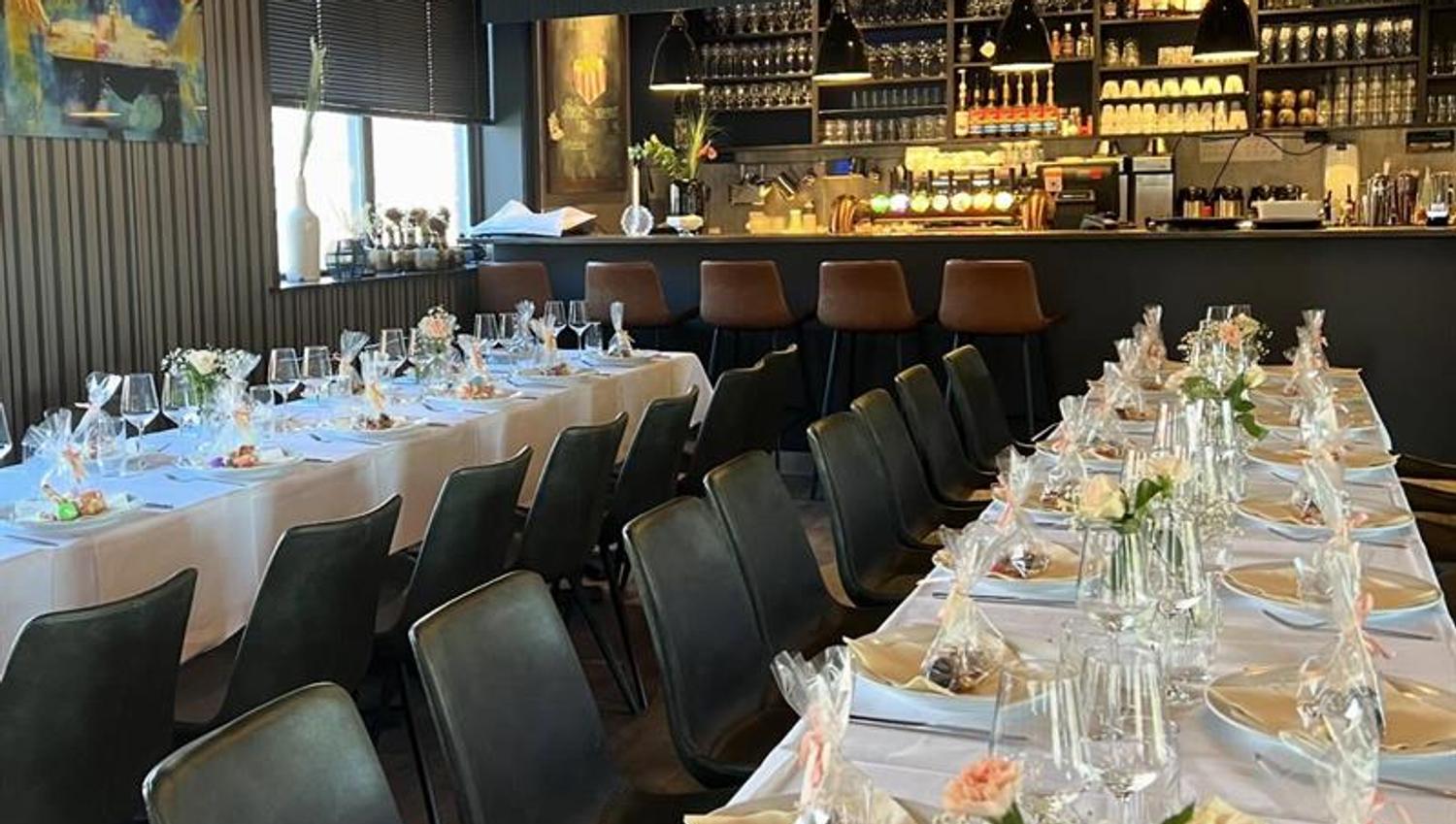 Dekket langbord inne i restauranten med glass, servietter og blomsterpynt. Vinhyller og mørke vegger skaper en elegant og intim atmosfære.
