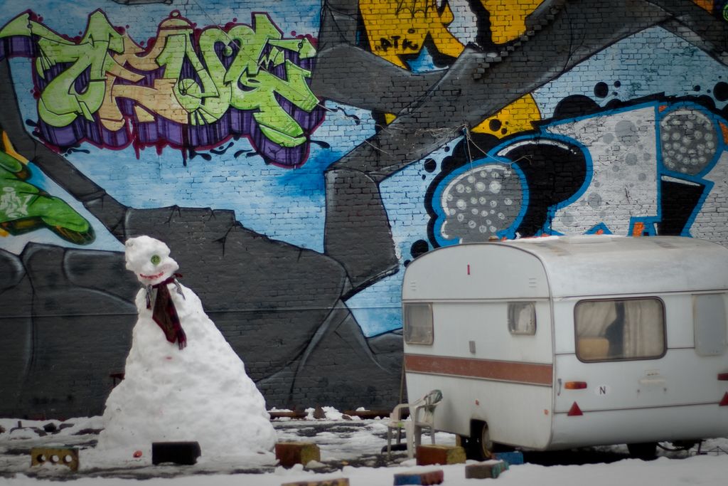 En snømann og en campingvogn foran en vegg med grafitti.