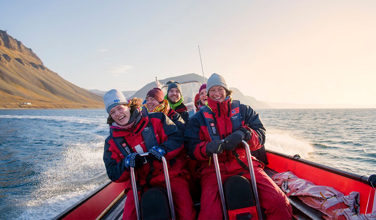 A group of guests on board a RIB boat sailing at speed in a fjord with mountains in the background