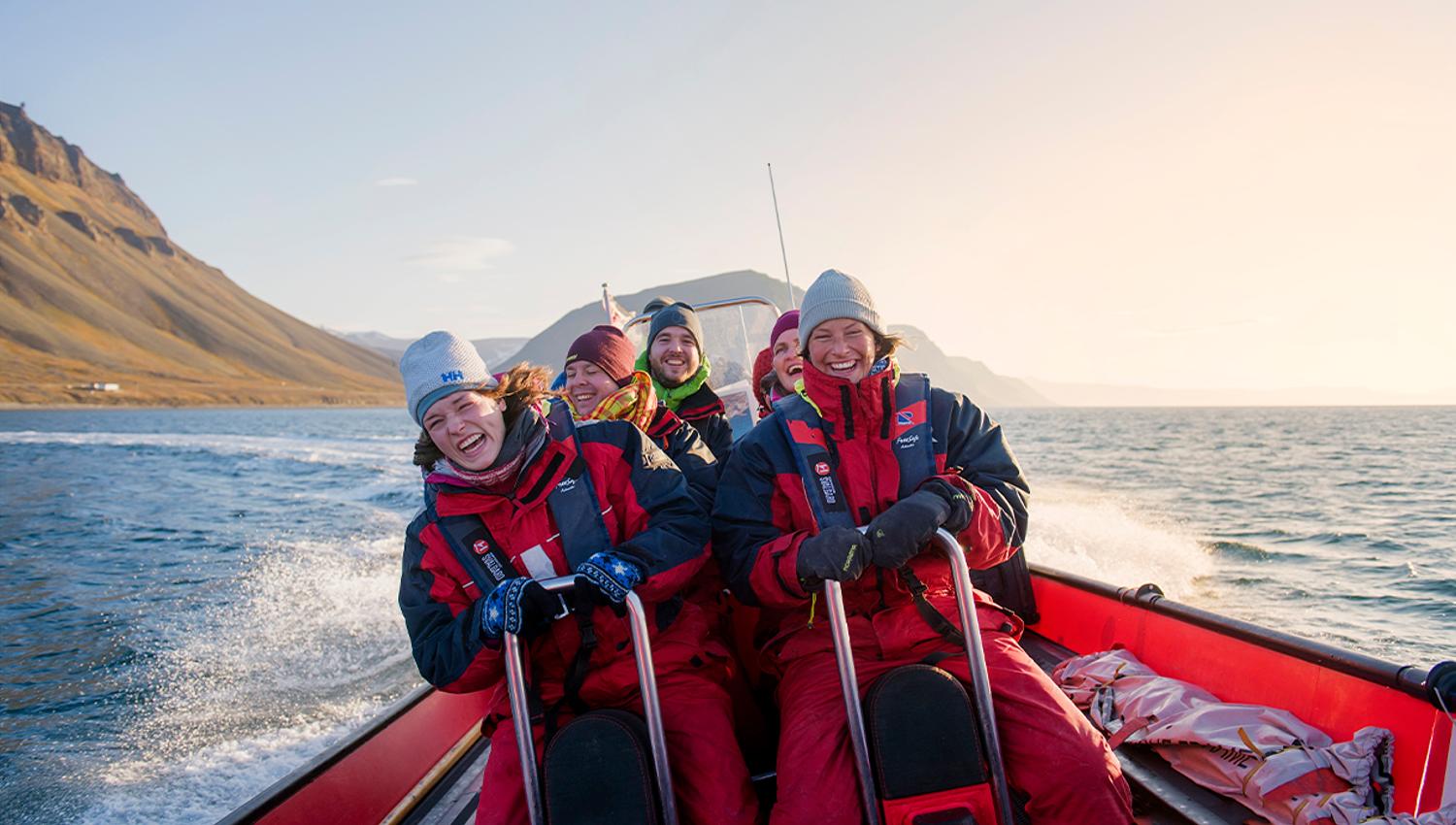 A group of guests on board a RIB boat sailing at speed in a fjord with mountains in the background