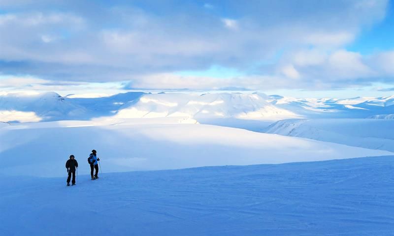 To gjester som går over en isbre og ser på utsikten mot et snødekt fjellandskap i bakgrunnen