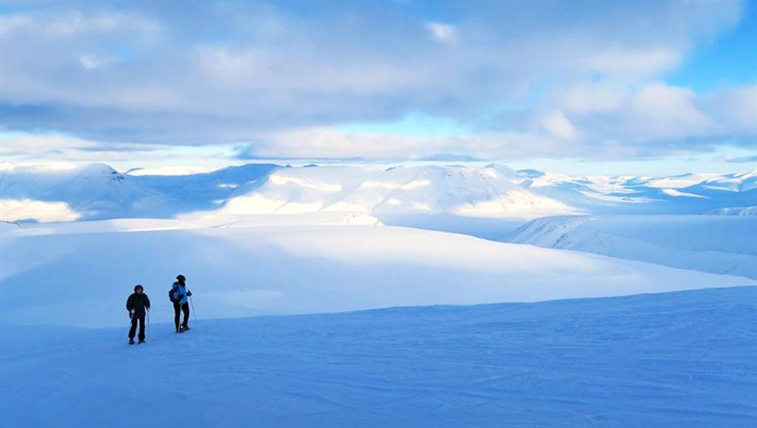 To gjester som går over en isbre og ser på utsikten mot et snødekt fjellandskap i bakgrunnen