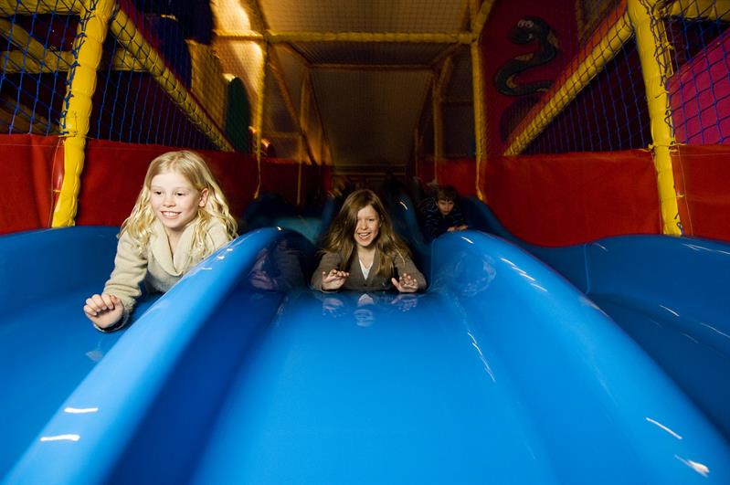 Children slide down on a blue slide. 