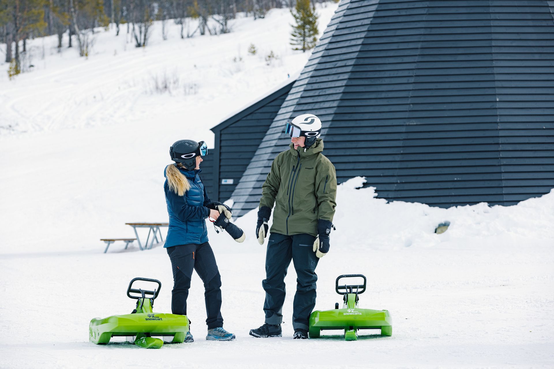 En gutt og ei jente snakker sammen foran de grønne akebrettene etter en fin tur i akebakken.