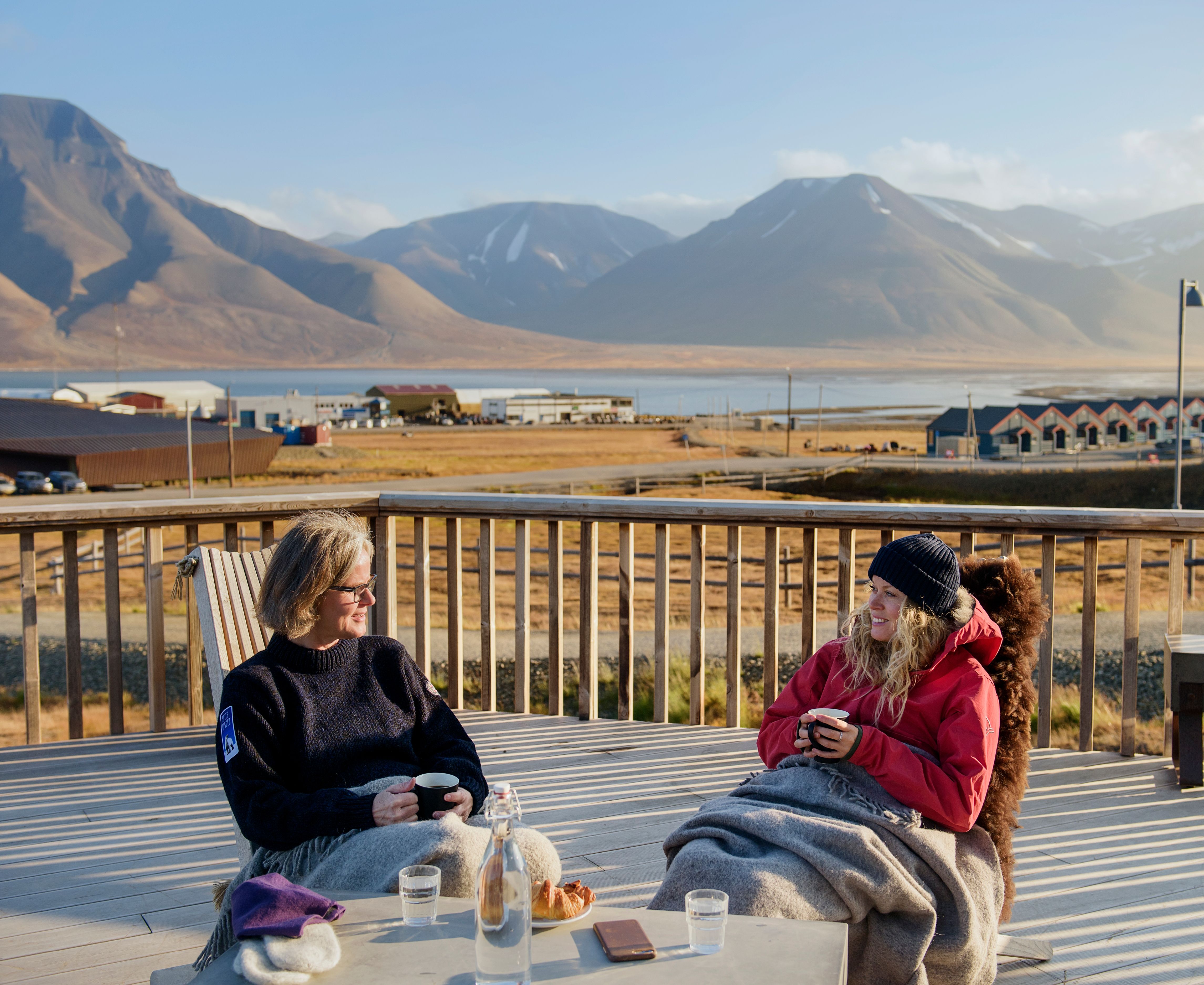Two guests sitting outdoors with blankets drinking coffee on a balcony