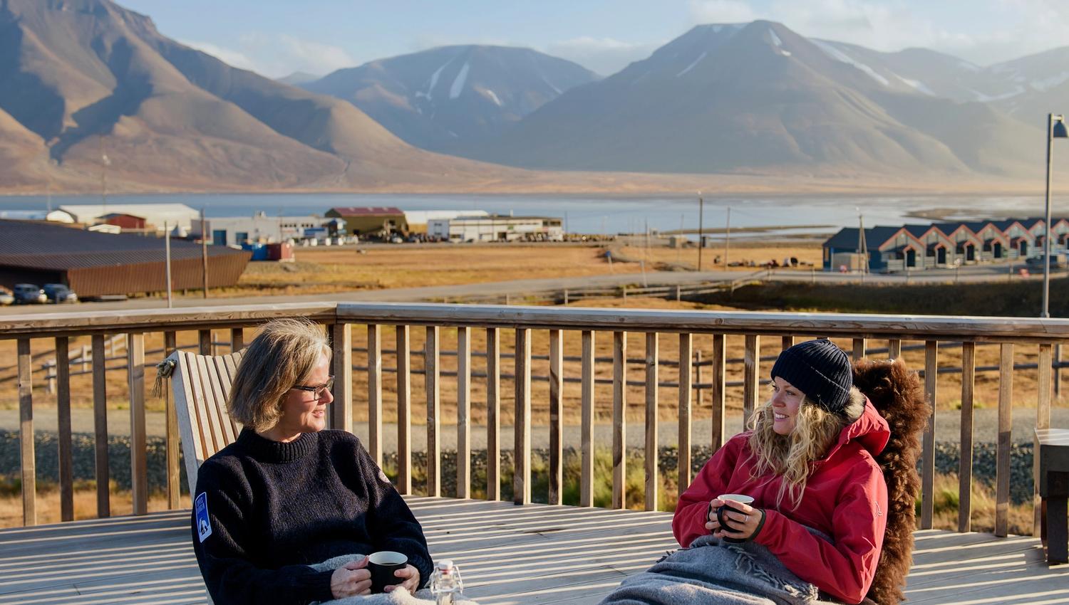 Two guests sitting outdoors with blankets drinking coffee on a balcony