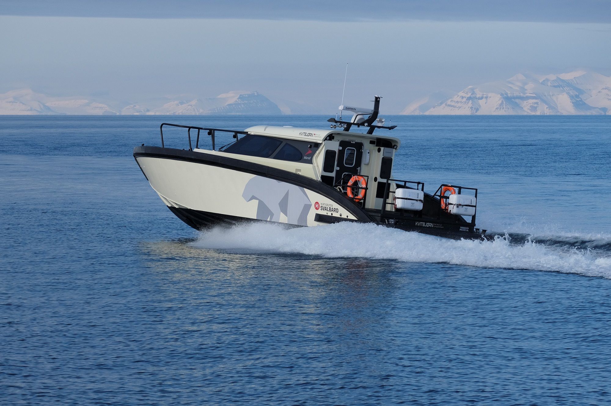 A boat (MS Kvitbjørn) sailing across a fjord with mountains in the background