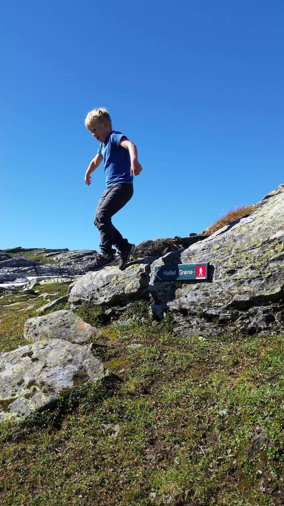 Barn leikar og hoppar på fjellet ved stiskilt til Hallet grøne i Hardanger.