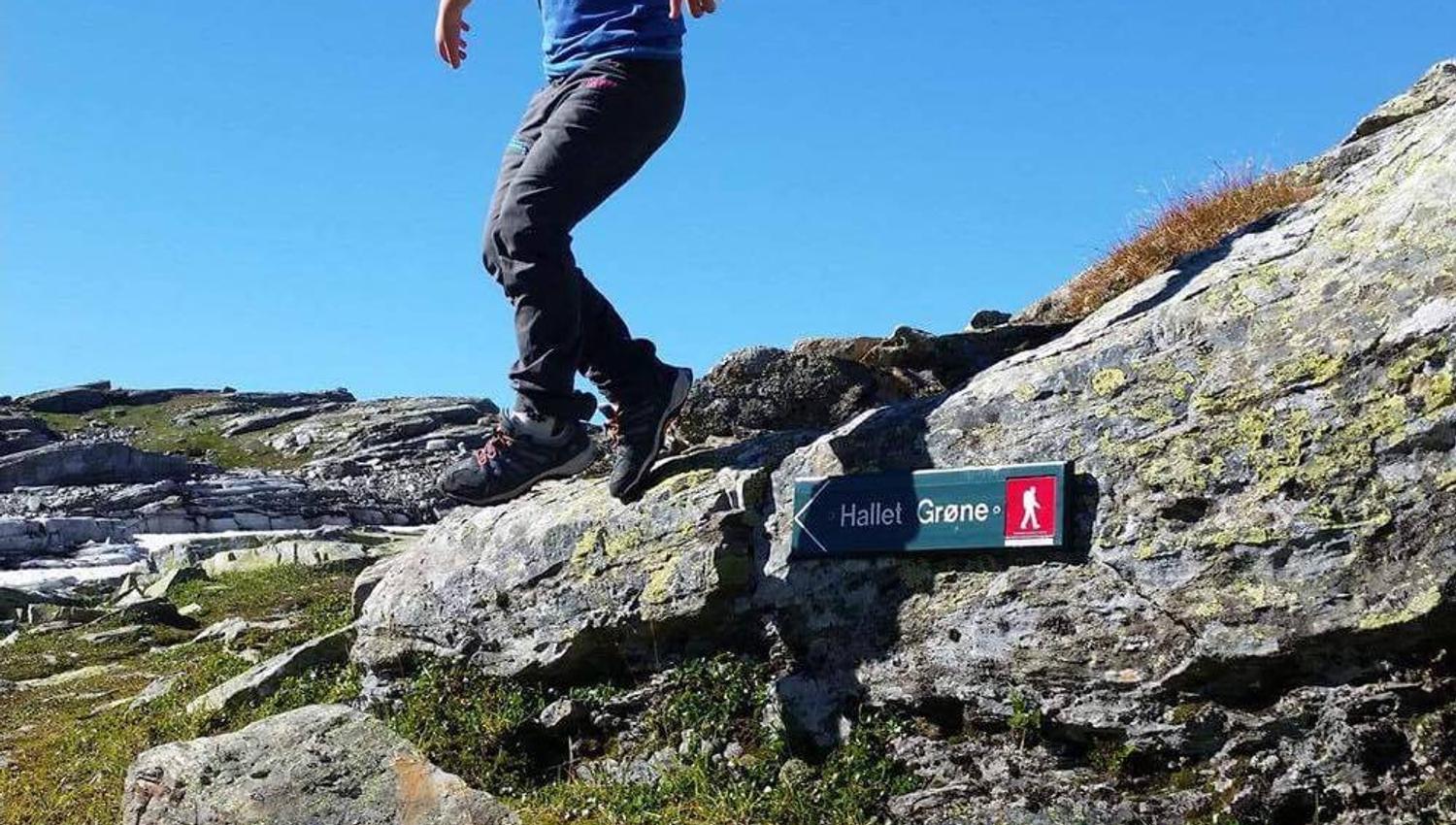 Barn leikar og hoppar på fjellet ved stiskilt til Hallet grøne i Hardanger.
