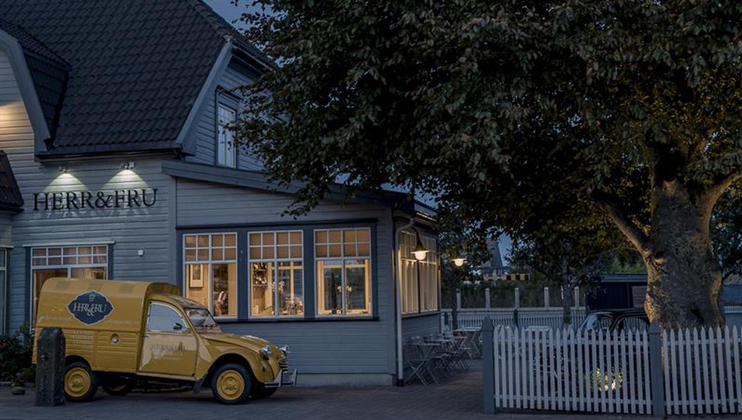 Fasade på kveldstid: grå restaurant. Gul leveringsbil parkert ved restauranten.