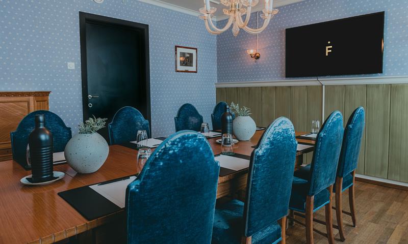 Et møterom med et bord, blå stoler og vegger, samt en skjerm