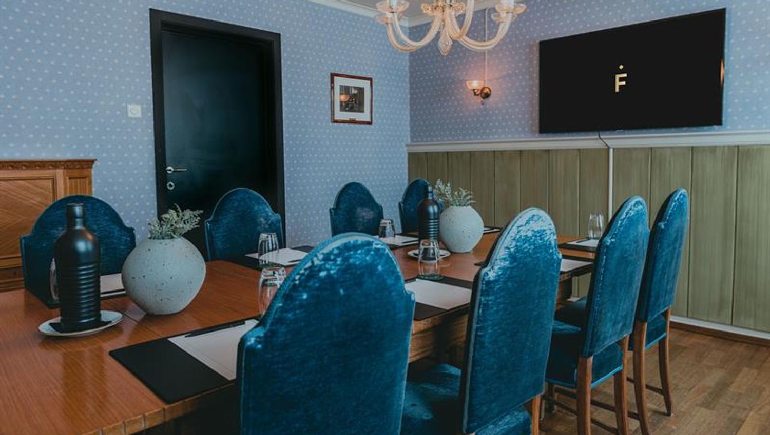 Et møterom med et bord, blå stoler og vegger, samt en skjerm