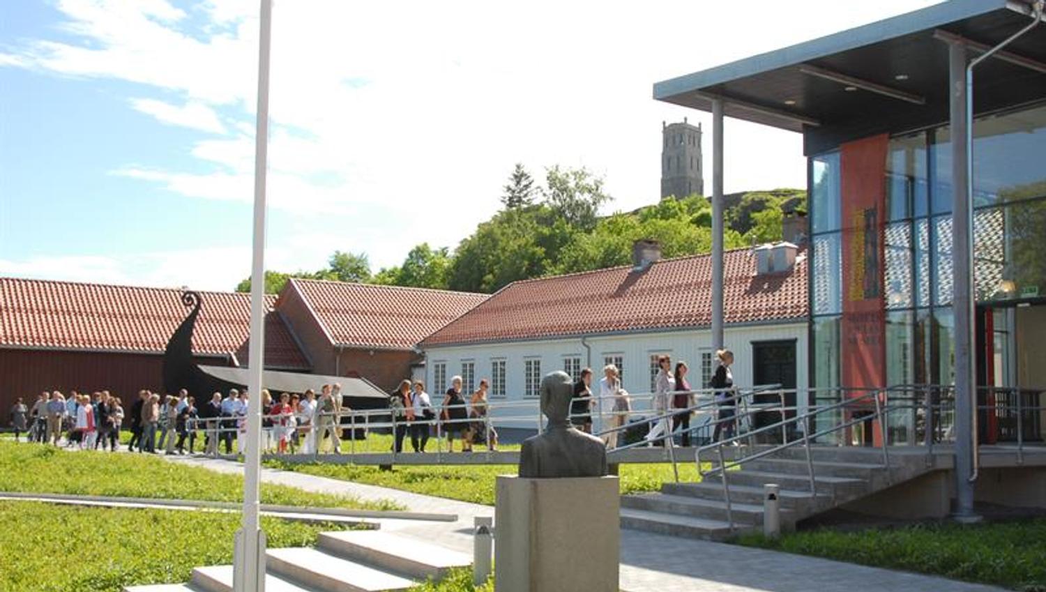 Hvitt trehus, glassbygning og mange mennesker som går inn på museet.