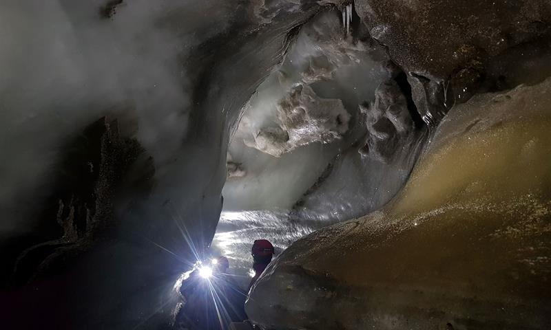 To personer med hodelykt i enden av en trang passasje i isgrotten.