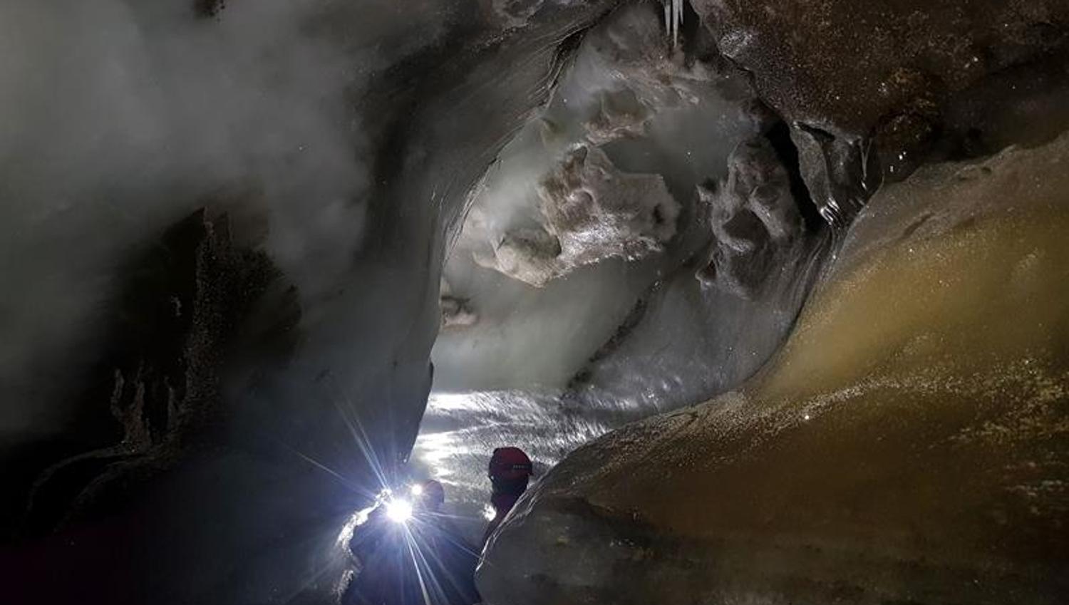 To personer med hodelykt i enden av en trang passasje i isgrotten.