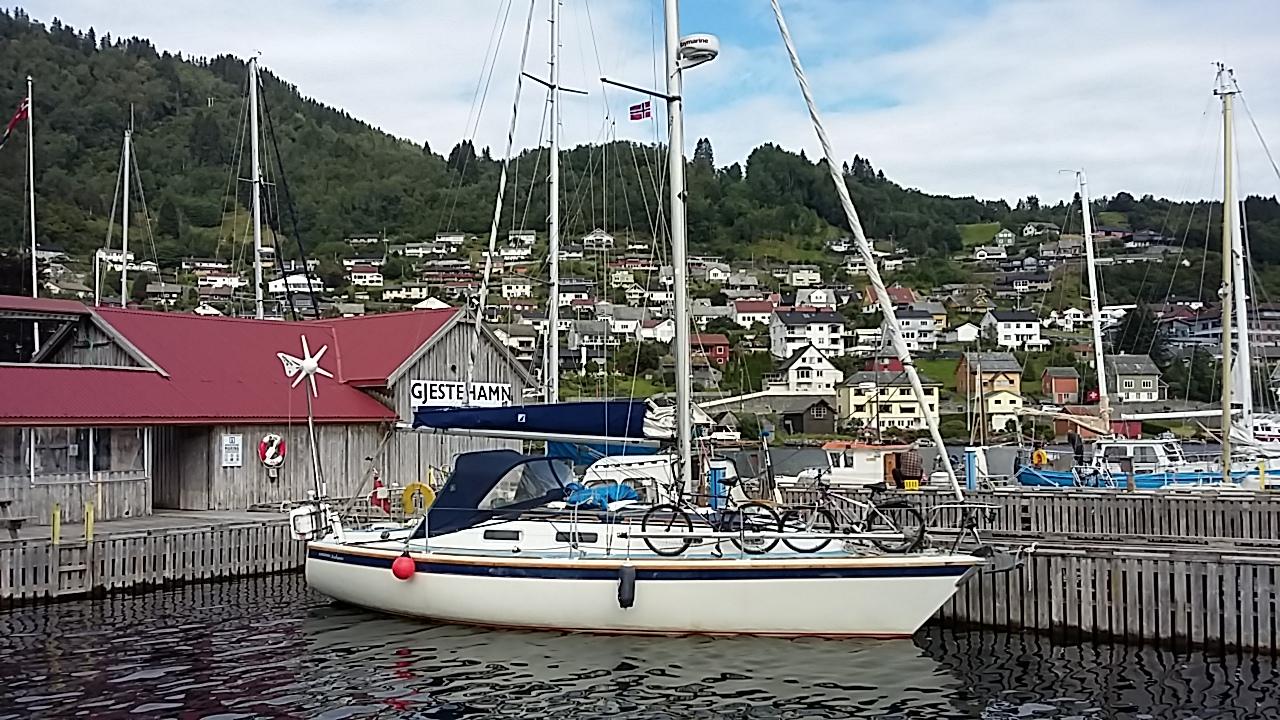 Sailboat moored at Norheimsund Guest Harbour, surrounded by wooden boathouses and fjordside mountains in Hardanger.