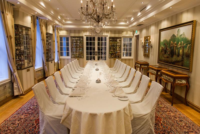Dekket langbord med hvit duk, stoler, malerier på veggene, lysekrone i taket