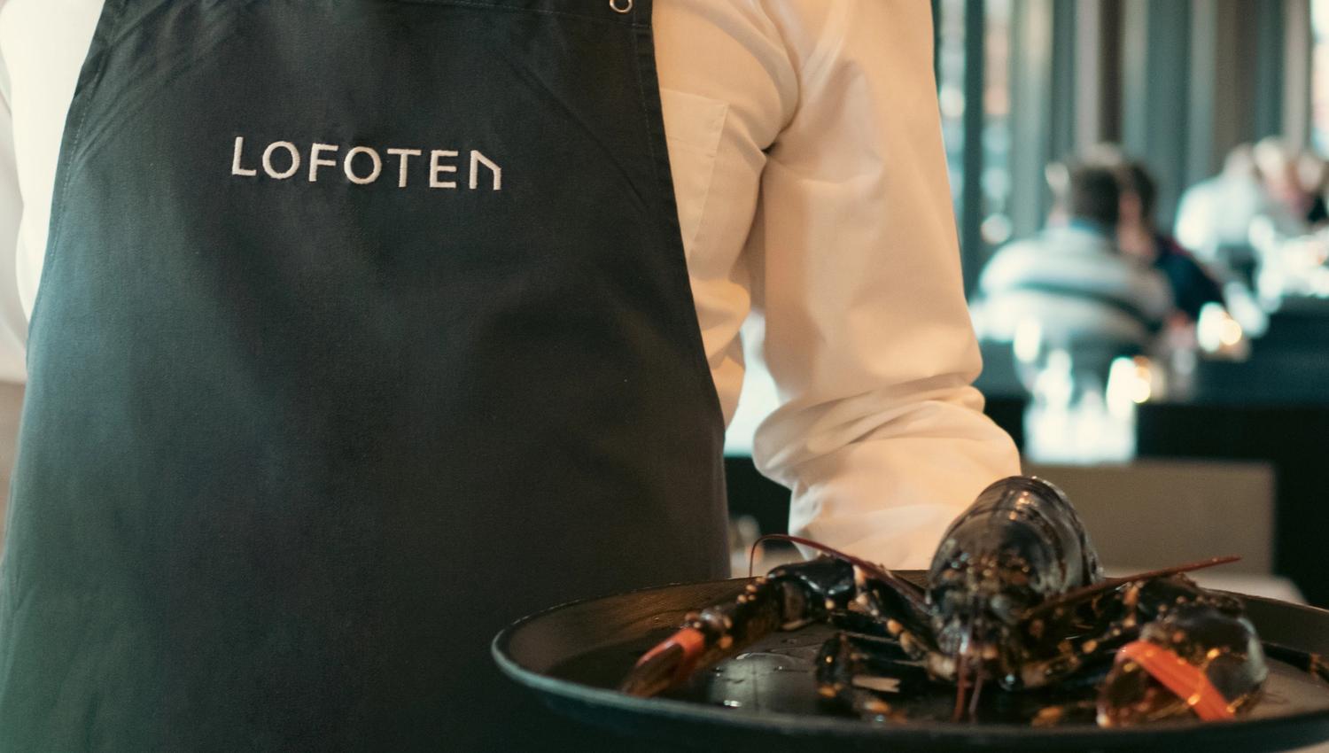 Mann i forkle som holder et brett med en hummer på