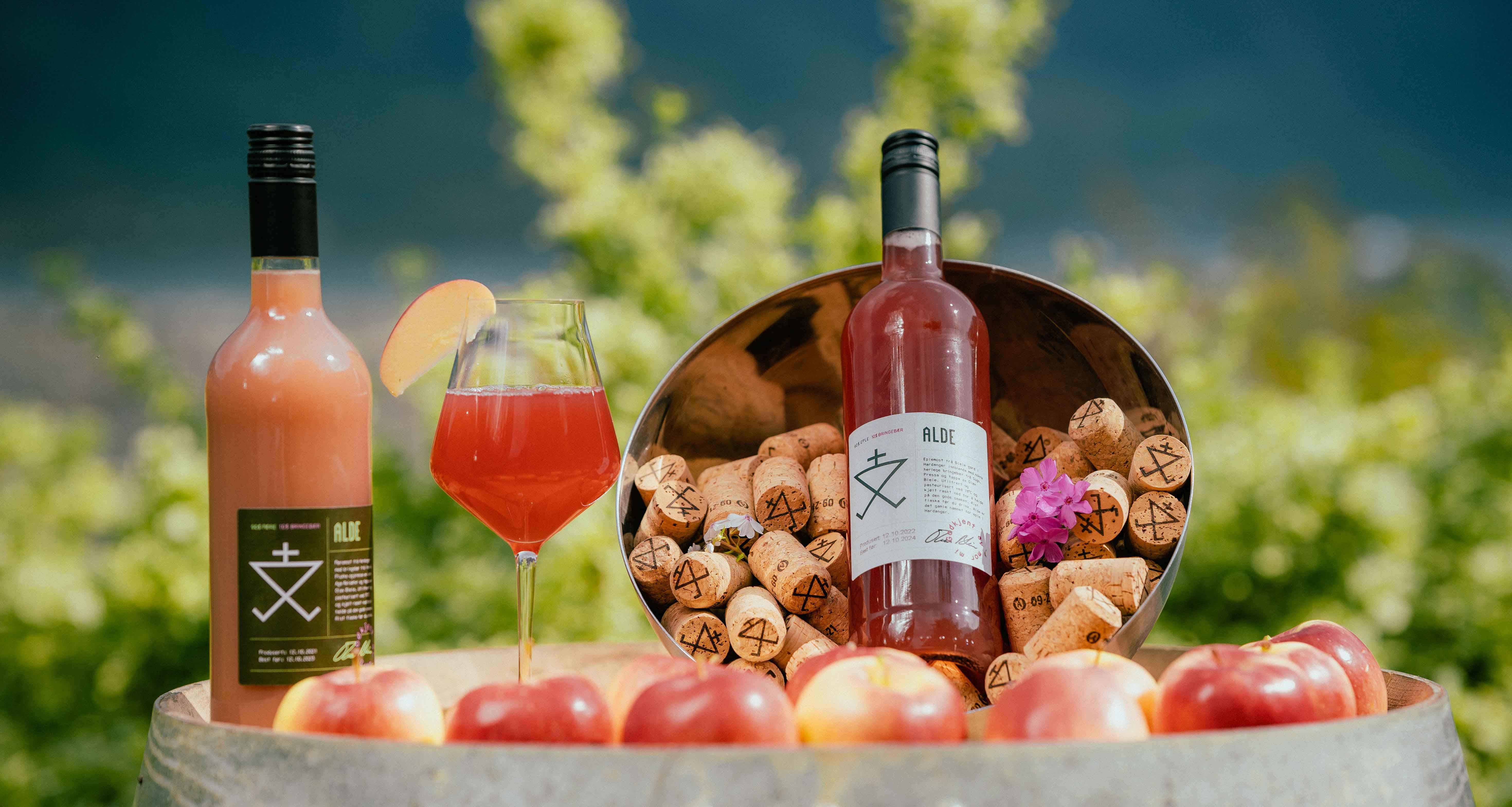 Flaske og glas med Alde eplemost omringa av eple og korkar i Hardanger.