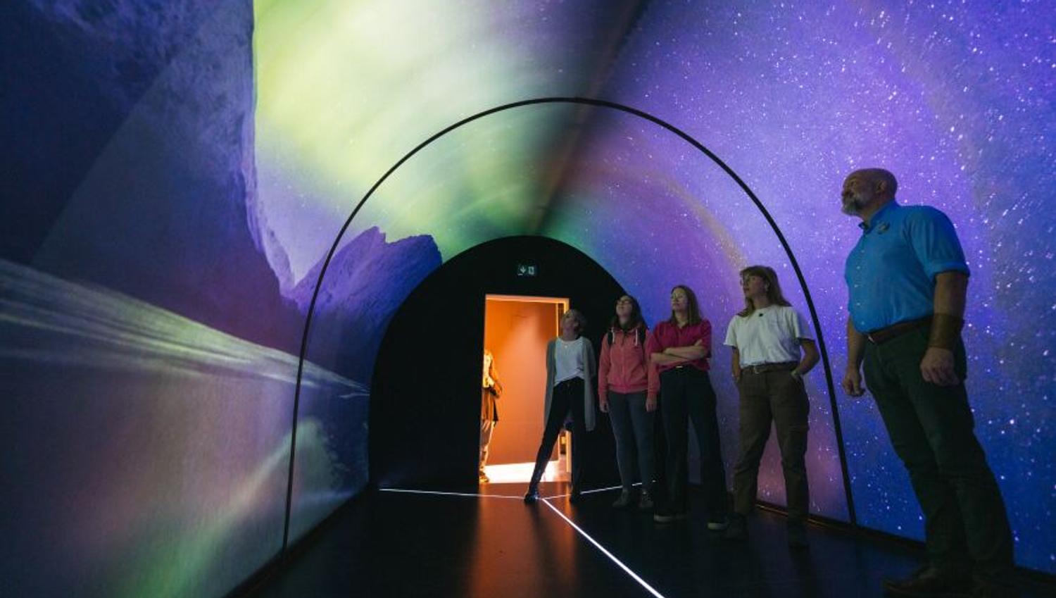 Fem personer i tunnel med nordlysprojeksjoner og stjernehimmel.