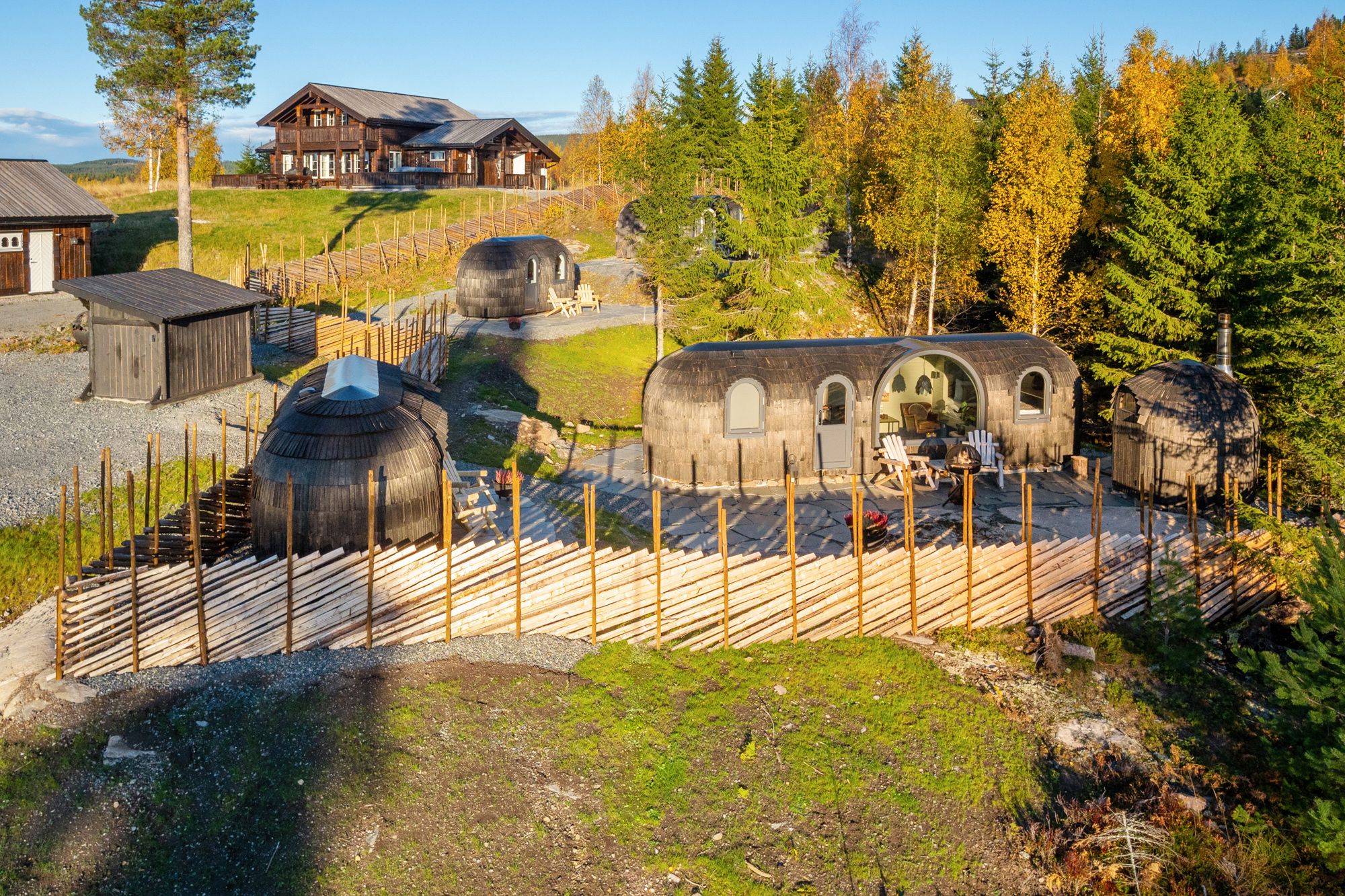 dronebilde av hytter med et gjerde og skog rundt