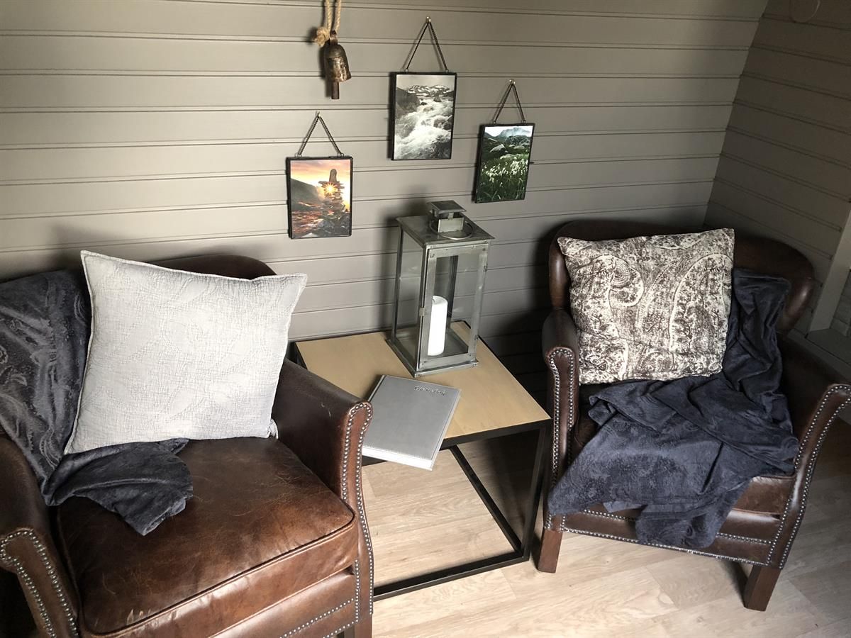 Small seating area with a chair, table, and décor inside a compact wooden cabin pod.