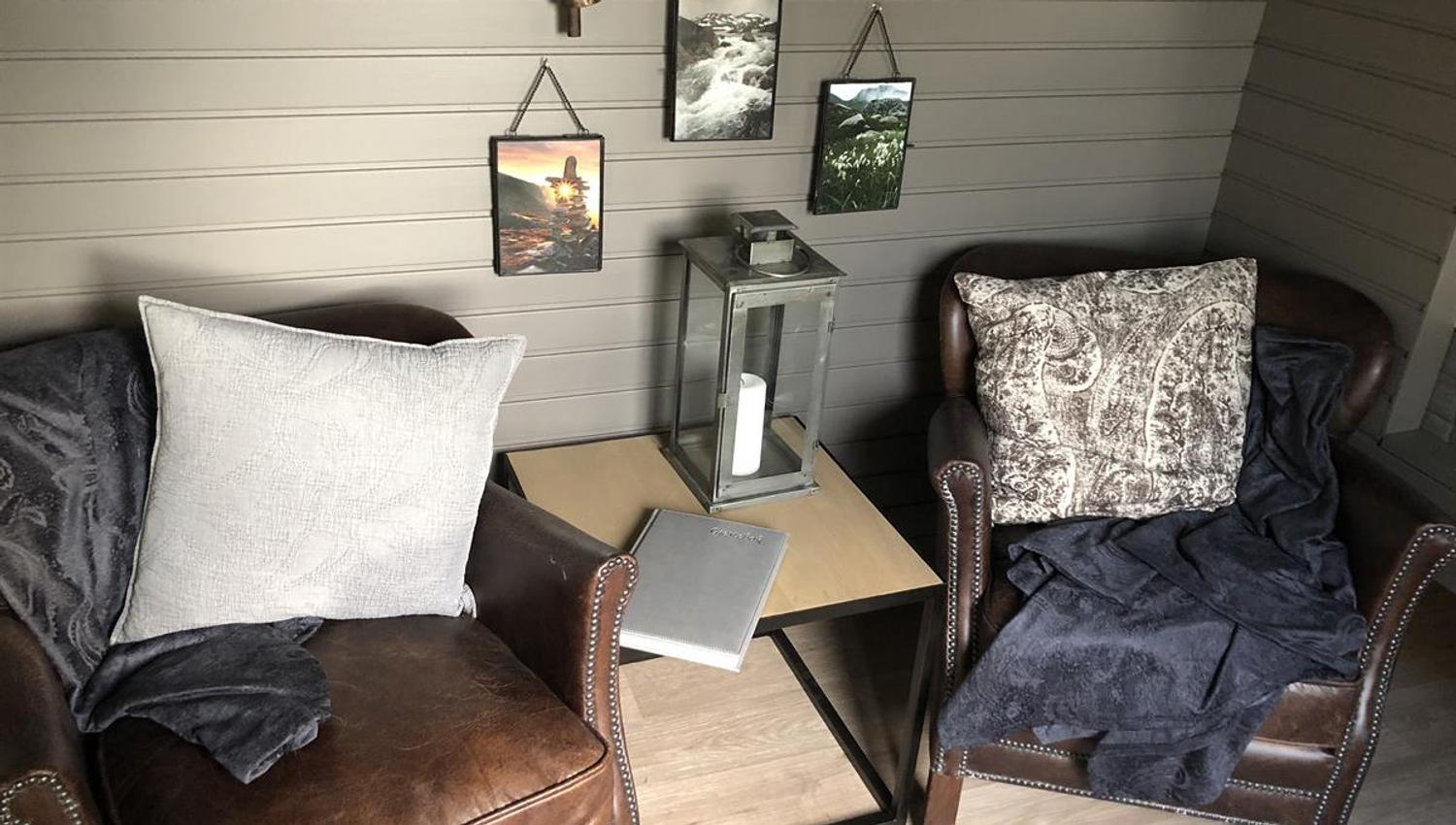 Small seating area with a chair, table, and décor inside a compact wooden cabin pod.
