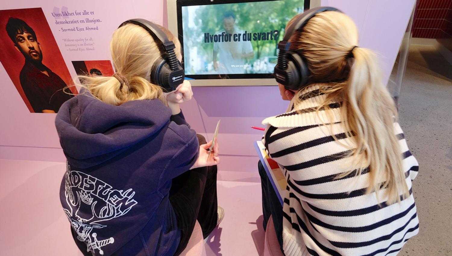 To jenter som ser på en video i en utstilling.