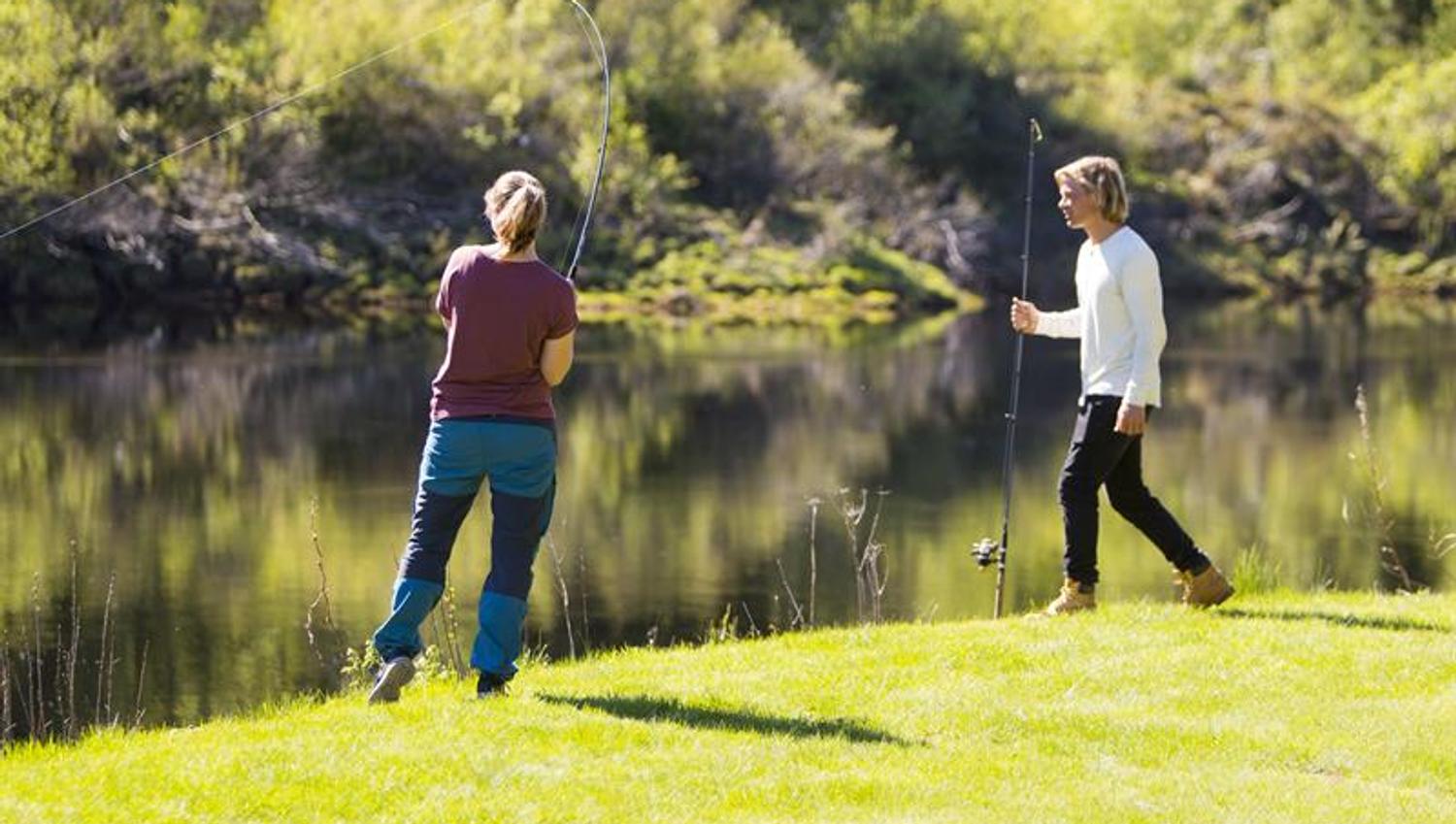 Par som står på gresset lang elva og fisker