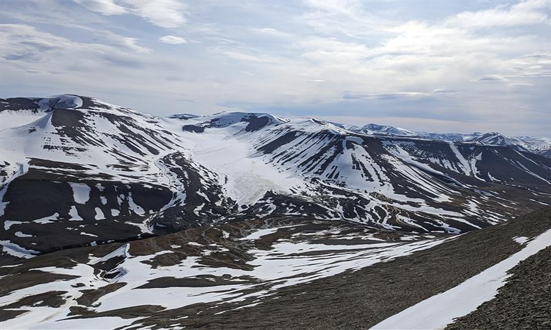 Et lett snødekt fjellandskap med en isbre og en skyet himmel i bakgrunnen