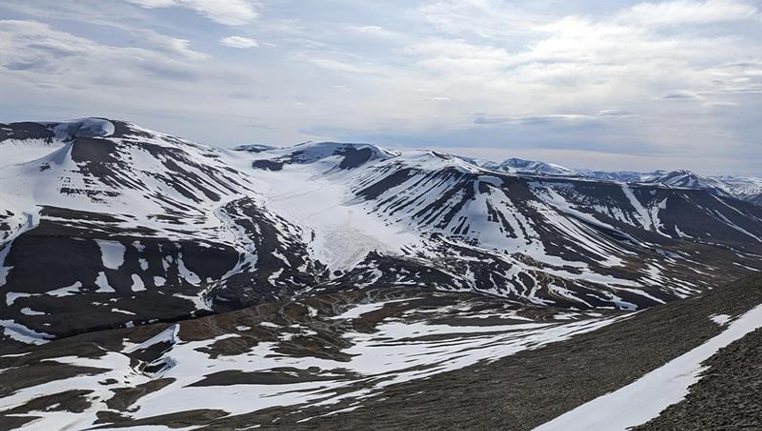 Et lett snødekt fjellandskap med en isbre og en skyet himmel i bakgrunnen
