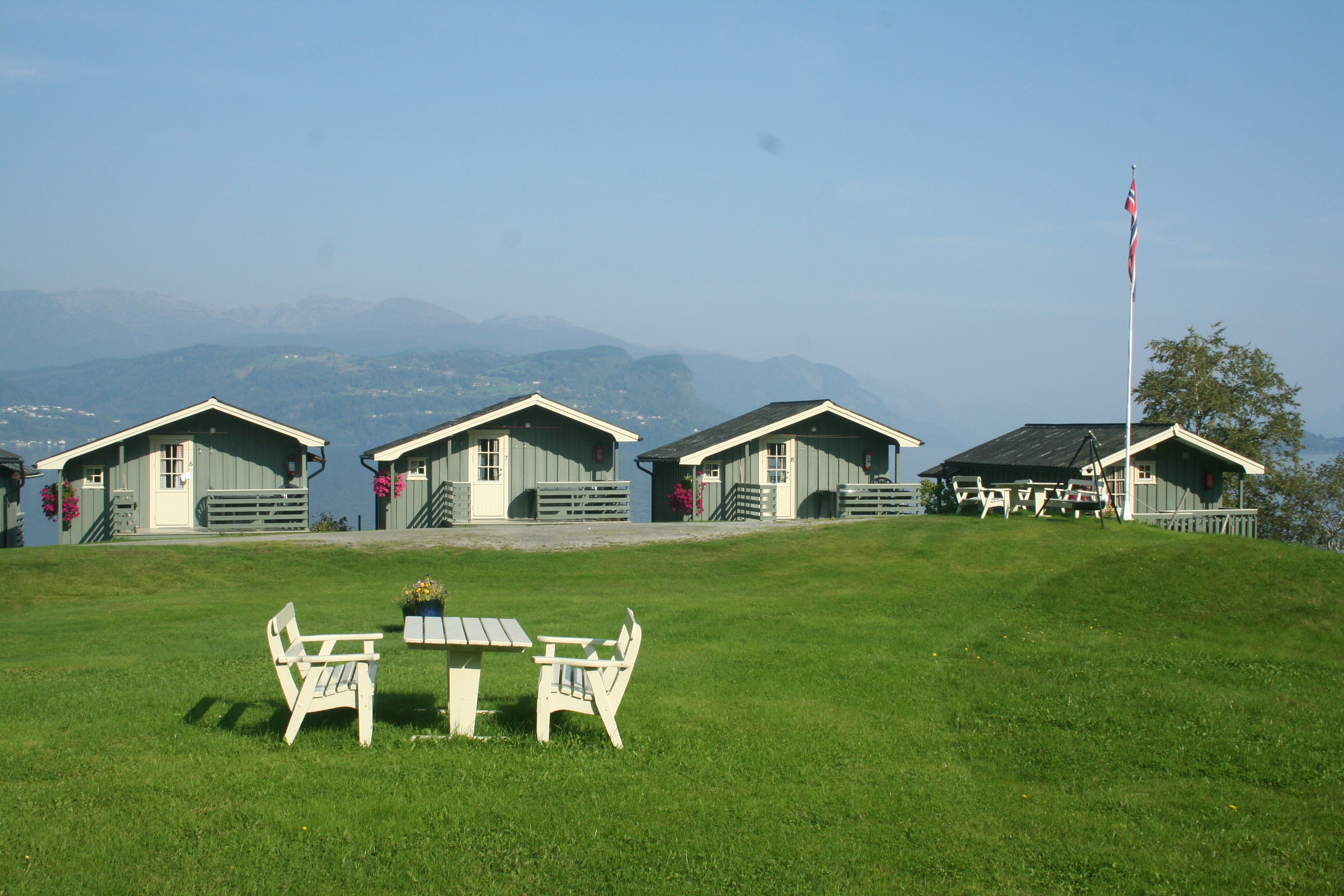 Grønt uteområde med sitjeplass og utsikt over hytter og fjord på Oddland Camping.