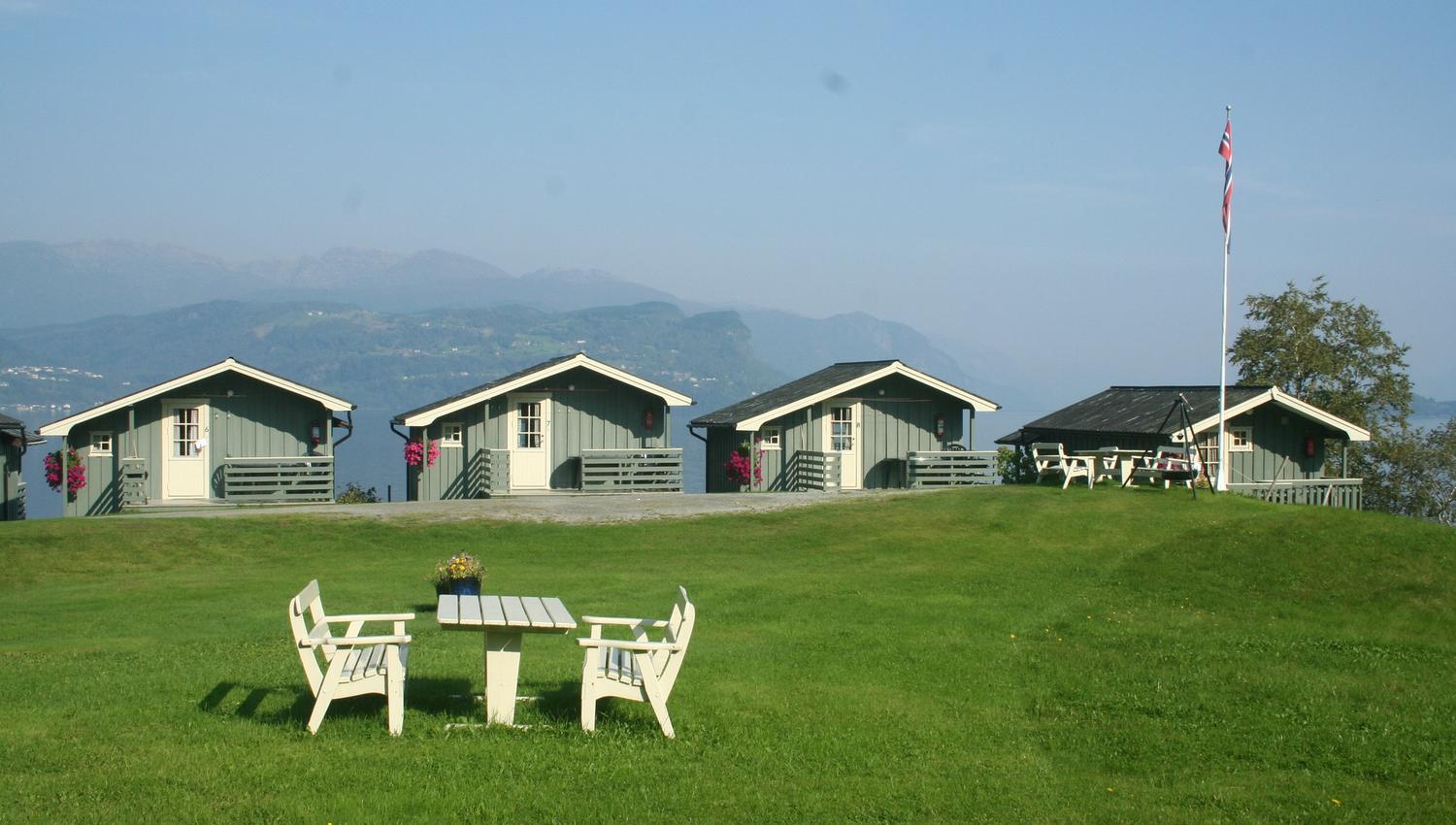 Grønt uteområde med sitjeplass og utsikt over hytter og fjord på Oddland Camping.