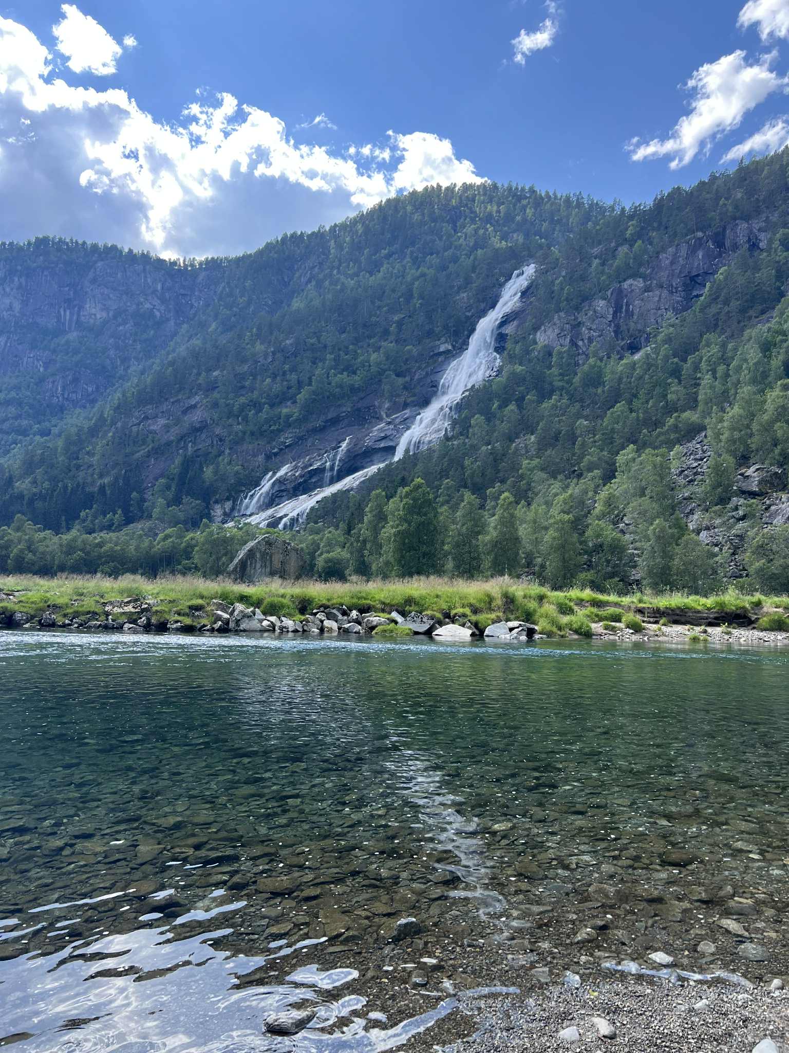 Telt og bubilar på grøne marker ved Hildal Camping med fossen i bakgrunnen.