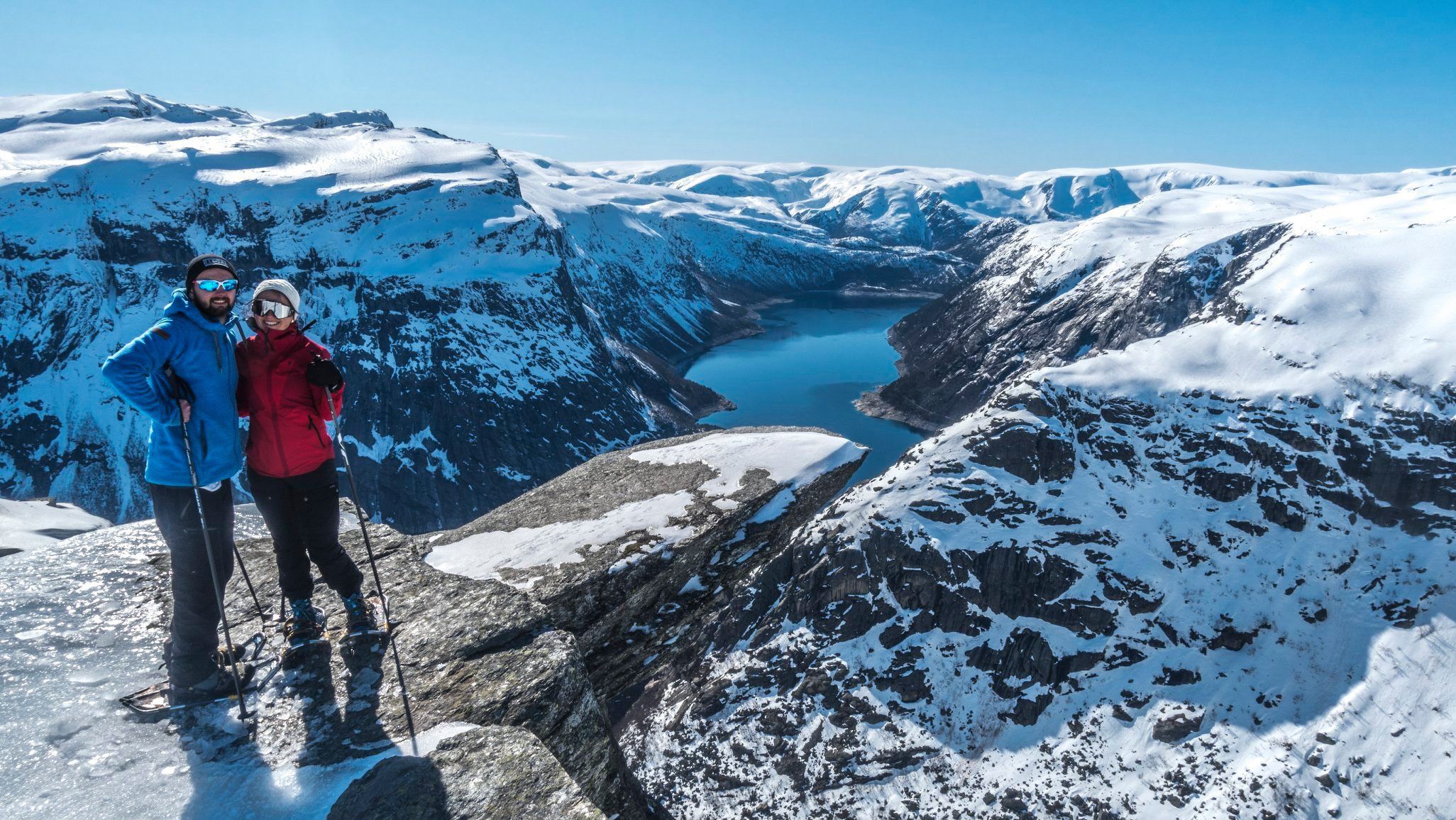 Couple with snowshoes standing on Trolltunga overlooking the icy fjord and mountains.
