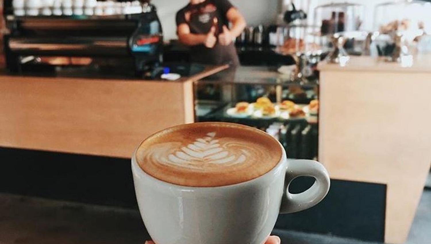 a hand holding up a coffee with the coffee shop in the background