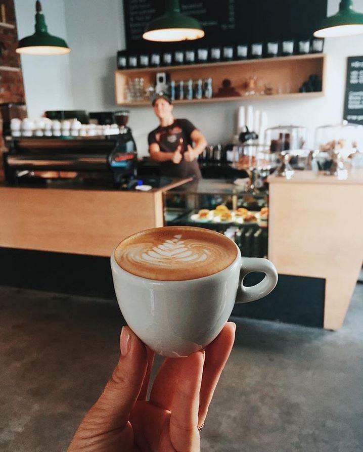 en hånd som viser frem en kaffe med kaffebaren i bakgrunnen
