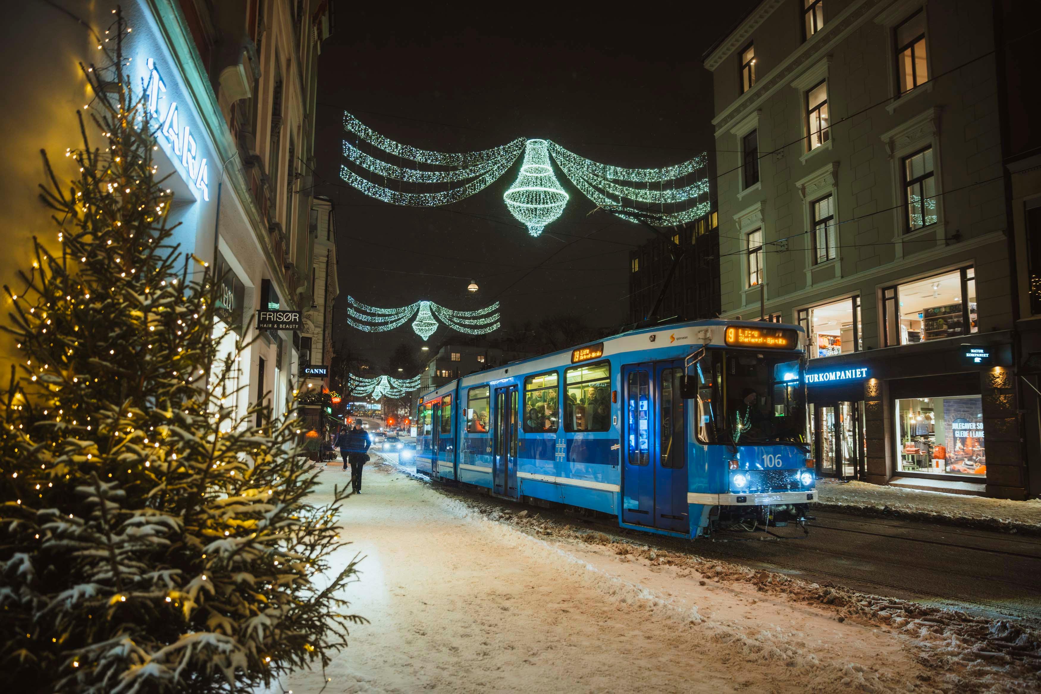 The tram gliding down Bogstadveien beneath the hanging Christmas lights.