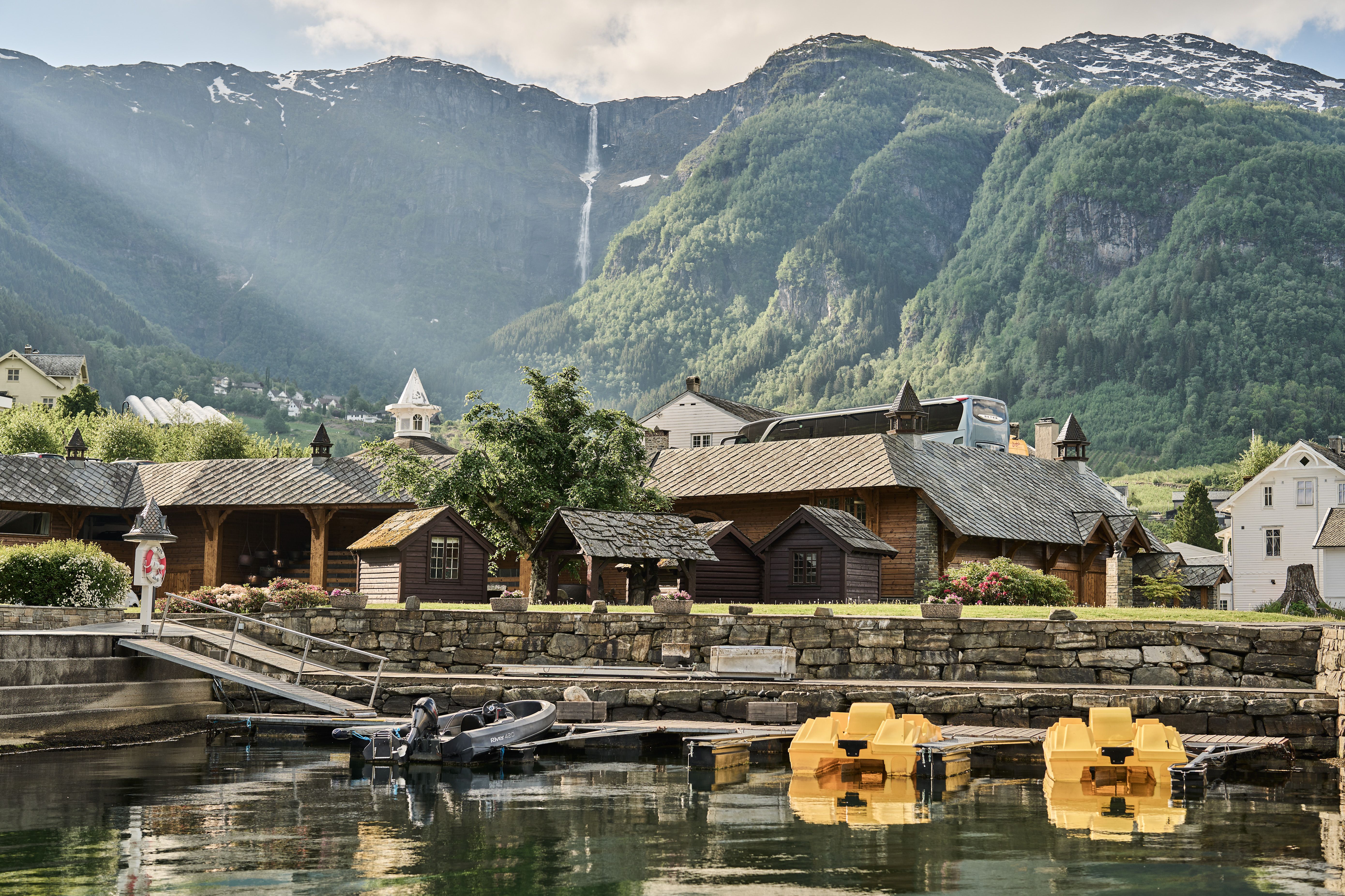 Utsikt mot båthamn og små hytter ved Hotel Ullensvang, med fjell i bakgrunnen.