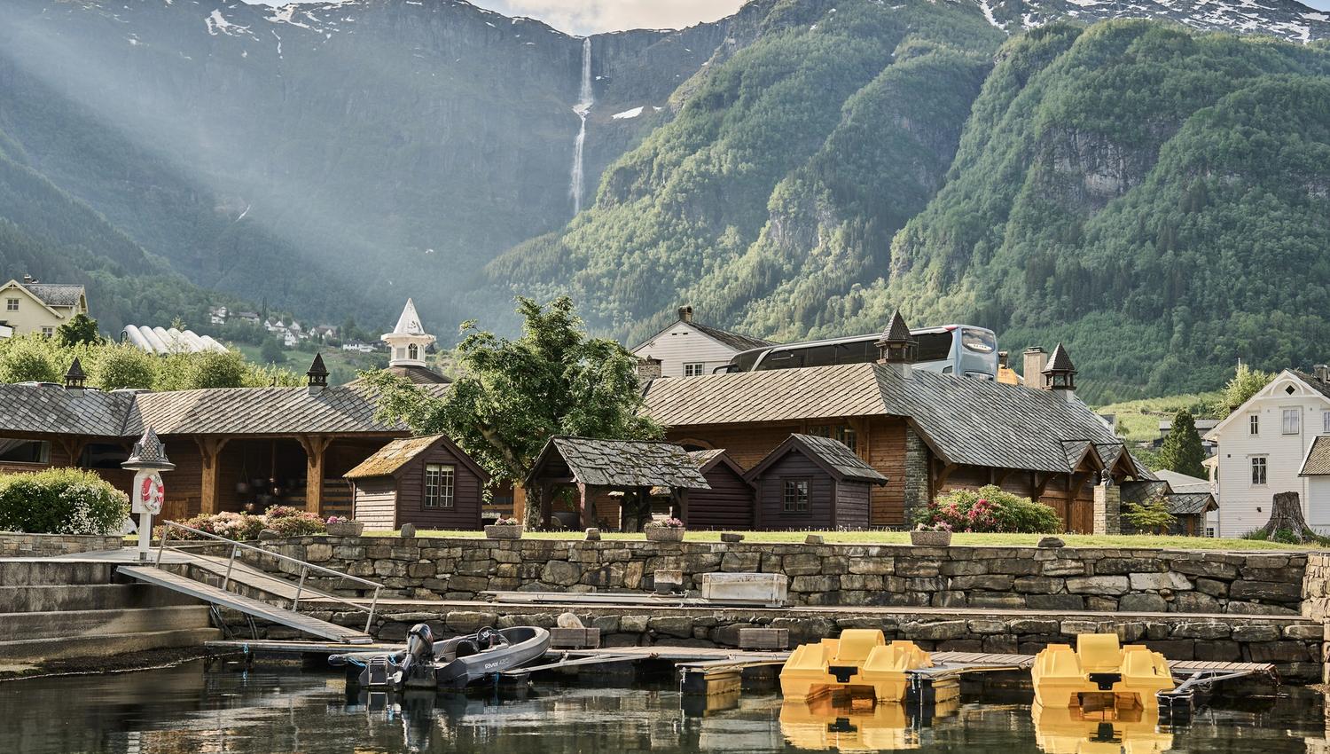 Utsikt mot båthamn og små hytter ved Hotel Ullensvang, med fjell i bakgrunnen.