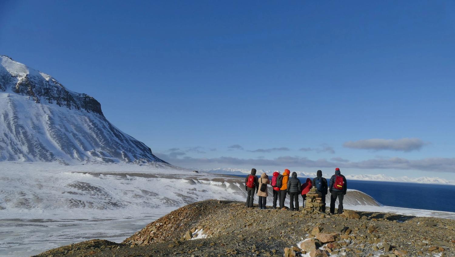 People on a small mountain looking out in the nature with snowcovered grounds and mountain in the background