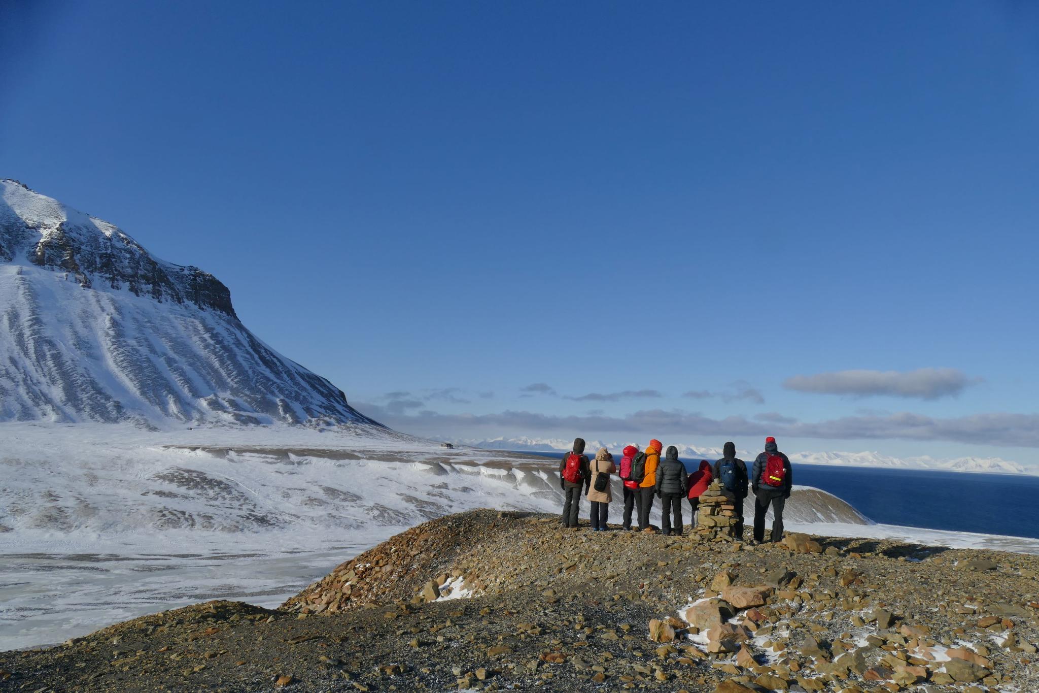 People on a small mountain looking out in the nature with snowcovered grounds and mountain in the background